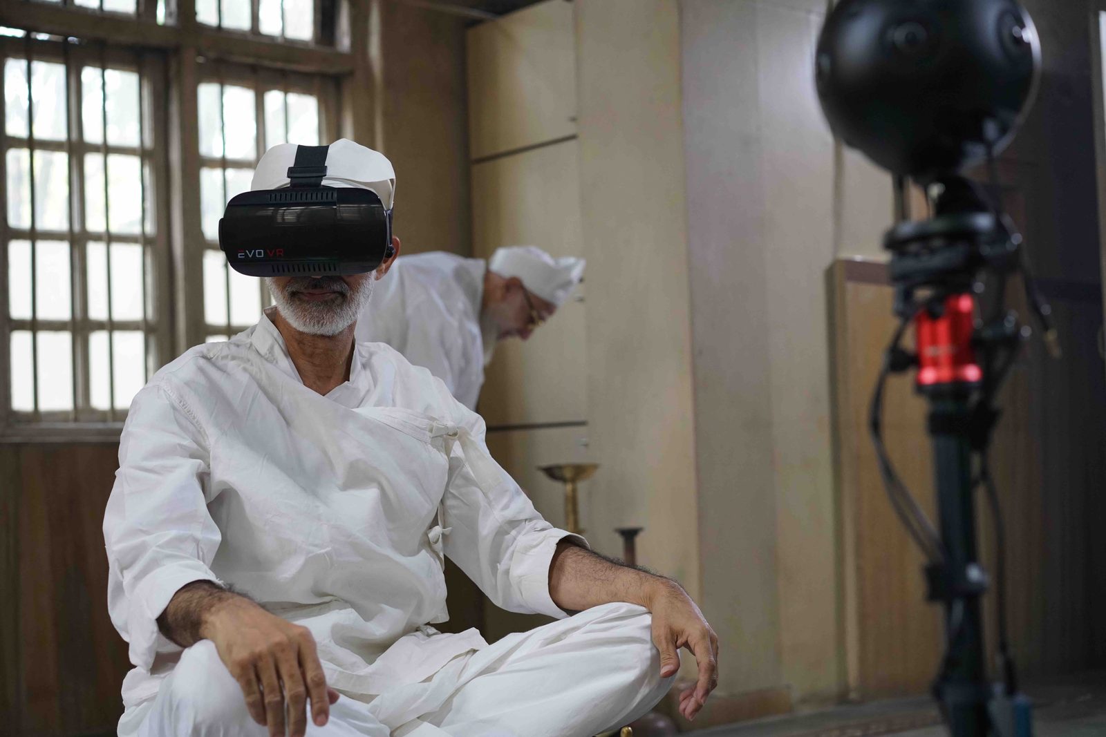 A priest wearing a VR headset beside a 360-degree camera rig inside the fire temple